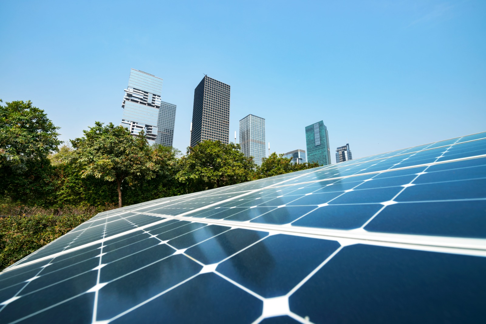 Solar panels in front of green trees and modern buildings. Property landlords are increasingly becoming infrastructure owners themselves, with buildings playing a significant and ever-growing role in energy generation.